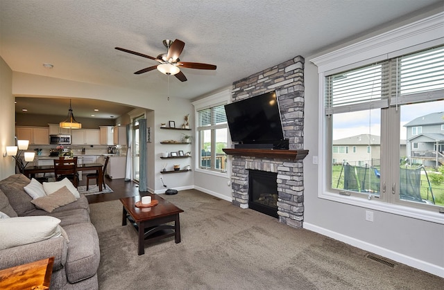 1880 Brodie St, Waukee, IA 50263 - living room with a ceiling fan, baseboards, a stone fireplace, a textured ceiling, and dark colored carpet
