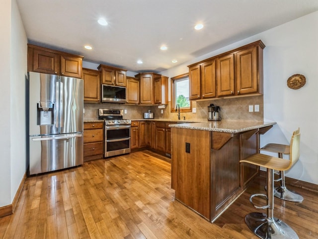 8305 Century Dr, West Des Moines, IA 50266 - kitchen with appliances with stainless steel finishes, brown cabinets, hardwood / wood-style flooring, a peninsula, and light stone counters