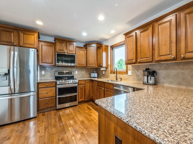 8305 Century Dr, West Des Moines, IA 50266 - kitchen with stainless steel appliances, brown cabinets, light stone countertops, light wood-style floors, and decorative backsplash