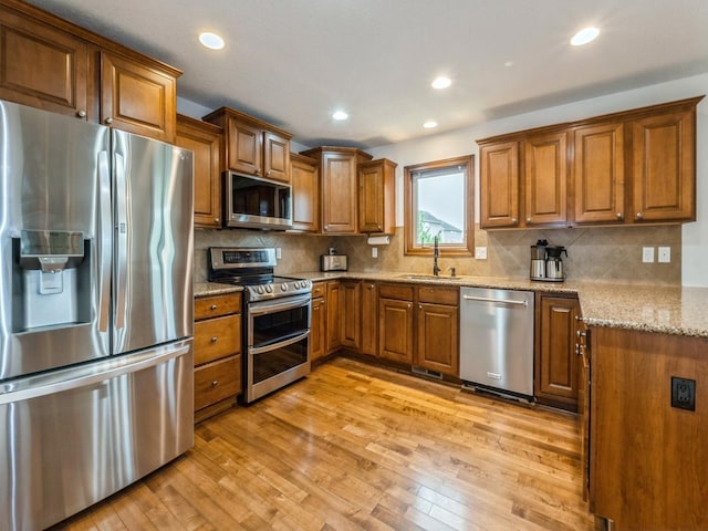 8305 Century Dr, West Des Moines, IA 50266 - kitchen with appliances with stainless steel finishes, brown cabinets, light stone countertops, light wood-style flooring, and recessed lighting