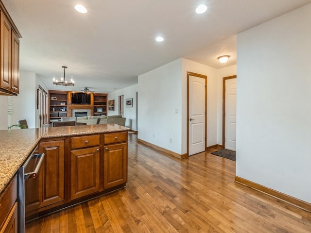 8305 Century Dr, West Des Moines, IA 50266 - kitchen featuring a fireplace, a chandelier, wood finished floors, a peninsula, and open floor plan