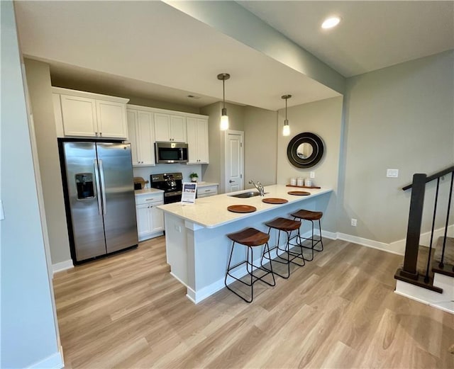5426 153rd St, Urbandale, IA 50323 - kitchen featuring appliances with stainless steel finishes, a sink, a breakfast bar, light wood-style flooring, and baseboards