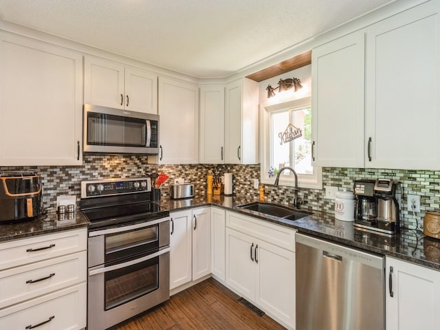 201 Cottage Ln, Montezuma, IA 50171 - kitchen with stainless steel appliances, a sink, backsplash, dark stone counters, and white cabinets