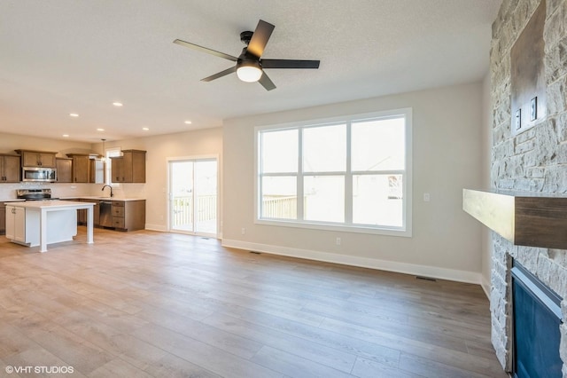 3418 5th Ave SE, Altoona, IA 50009 - unfurnished living room with a ceiling fan, baseboards, light wood-style flooring, a stone fireplace, and a sink