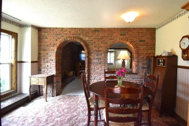 231 S 1st St, Ogden, IA 50212 - carpeted dining space featuring a textured ceiling, arched walkways, and brick wall