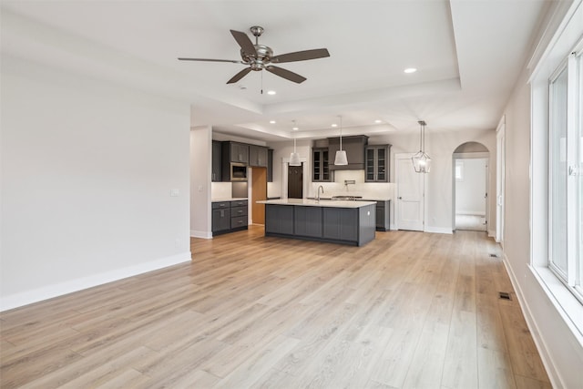 17829 Valley View Dr, Clive, IA 50325 - kitchen featuring a tray ceiling, arched walkways, light countertops, a ceiling fan, and light wood-type flooring