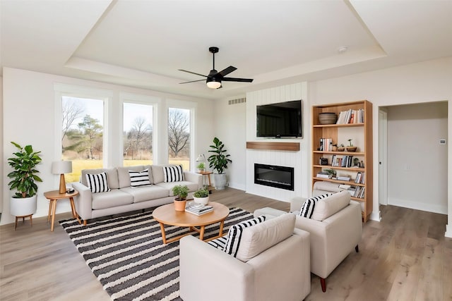 733 17th Ave SE, Altoona, IA 50009 - living room featuring a tray ceiling, ceiling fan, a large fireplace, and light wood-style floors