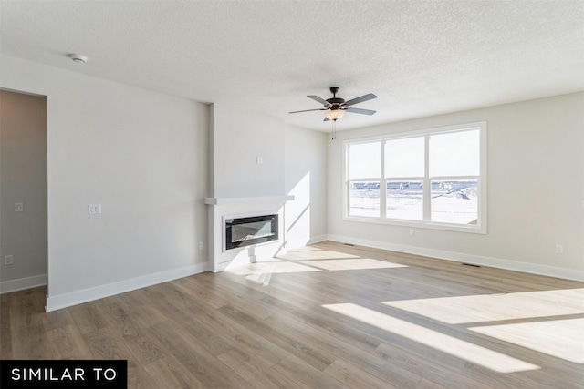 4208 NE 5th St, Ankeny, IA 50021 - unfurnished living room with a glass covered fireplace, wood finished floors, a textured ceiling, ceiling fan, and baseboards