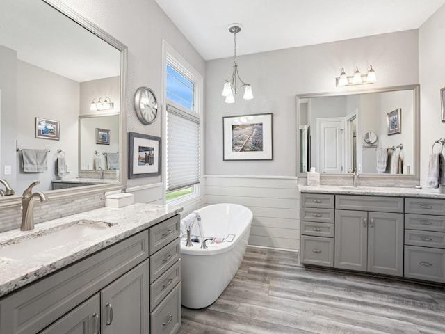 15075 Sheridan Ave, Clive, IA 50325 - full bathroom with two vanities, wood finished floors, a freestanding tub, wainscoting, and a chandelier