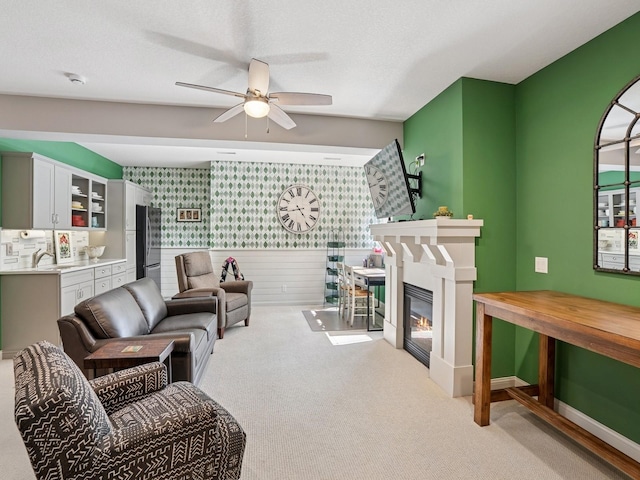 15075 Sheridan Ave, Clive, IA 50325 - carpeted living room featuring wallpapered walls, a ceiling fan, wainscoting, a sink, and a glass covered fireplace