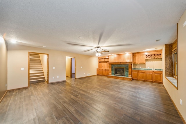 8148 Durham Cir, Johnston, IA 50131 - unfurnished living room featuring dark wood finished floors, stairs, a ceiling fan, a fireplace with raised hearth, and a textured ceiling