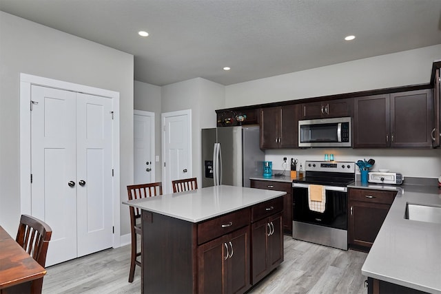 2930 Kestrel St, Norwalk, IA 50211 - kitchen featuring appliances with stainless steel finishes, light wood-type flooring, dark brown cabinets, a breakfast bar area, and recessed lighting