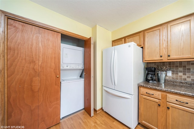 312 NE Harvey St, Grimes, IA 50111 - kitchen with freestanding refrigerator, stacked washing machine and dryer, light wood finished floors, decorative backsplash, and dark stone countertops