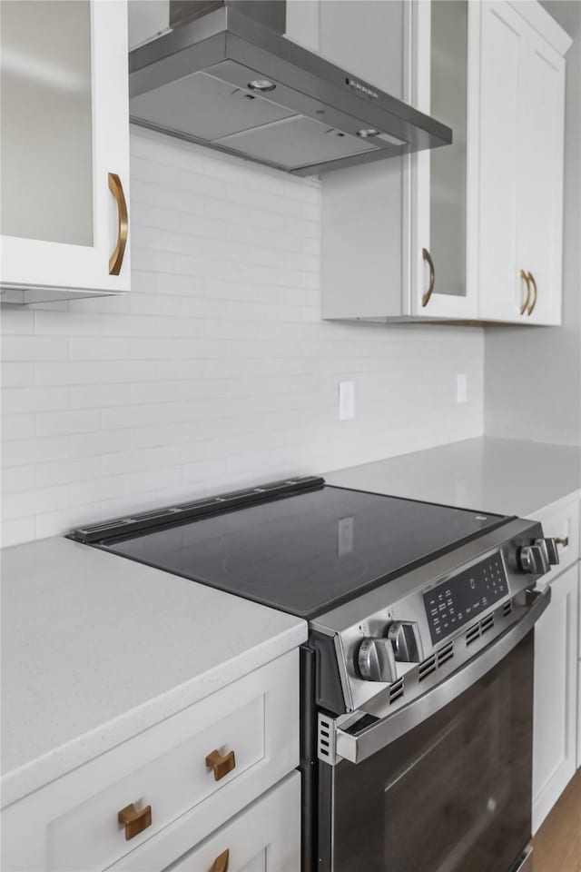 1201 Lakeview Cir NW, Bondurant, IA 50035 - kitchen featuring stainless steel electric range, wall chimney range hood, decorative backsplash, white cabinets, and glass insert cabinets