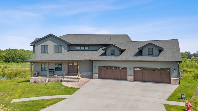100 Coventry Ct, Clear Lake, IA 50428 - modern farmhouse featuring covered porch, a front lawn, driveway, a shingled roof, and stone siding