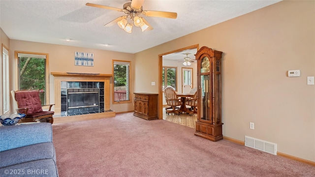 1105 E Henderson Pl, Indianola, IA 50125 - living area featuring ceiling fan, a tiled fireplace, carpet flooring, a textured ceiling, and baseboards