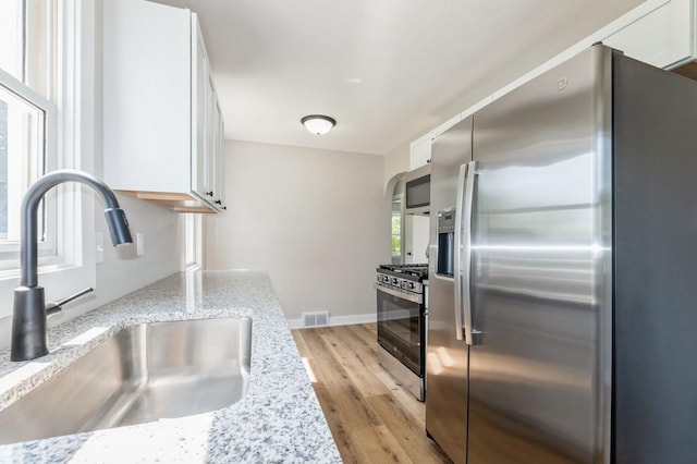 3811 E 30th St, Des Moines, IA 50317 - kitchen featuring appliances with stainless steel finishes, a sink, white cabinetry, light wood-style floors, and light stone counters