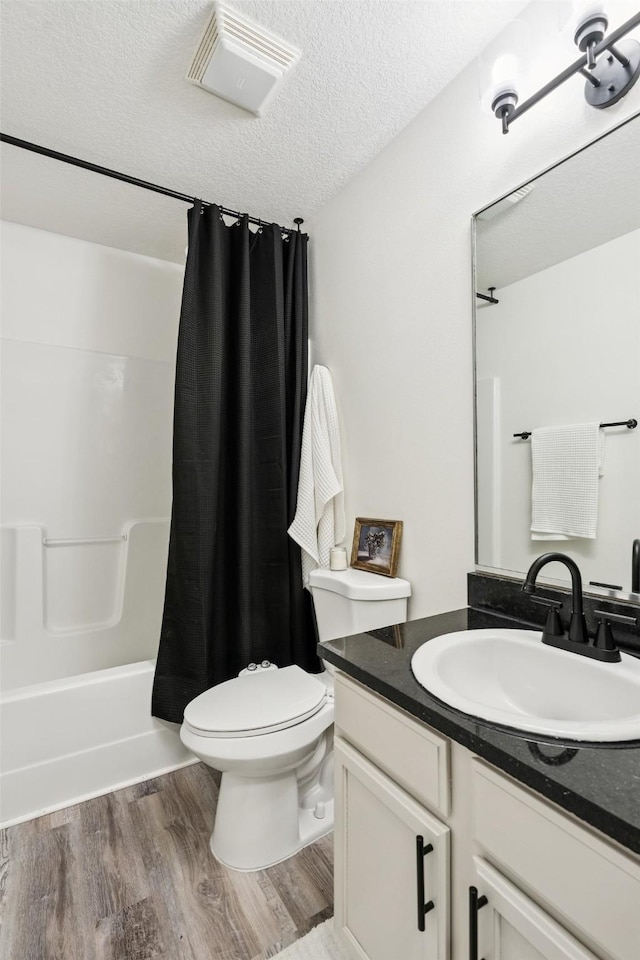 2150 NE 18th St Unit 101, Grimes, IA 50111 - bathroom featuring vanity, wood finished floors, toilet, a textured ceiling, and shower / bathtub combination with curtain