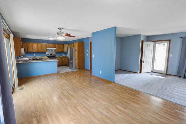 102 Jackson St, Pella, IA 50219 - kitchen with appliances with stainless steel finishes, open floor plan, a sink, brown cabinetry, and a textured ceiling
