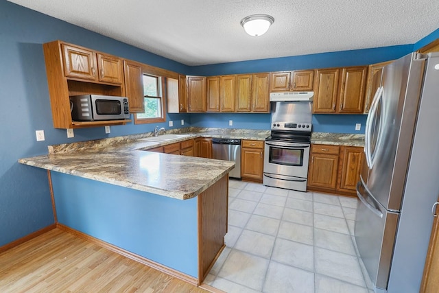 102 Jackson St, Pella, IA 50219 - kitchen with appliances with stainless steel finishes, under cabinet range hood, a sink, a peninsula, and brown cabinets