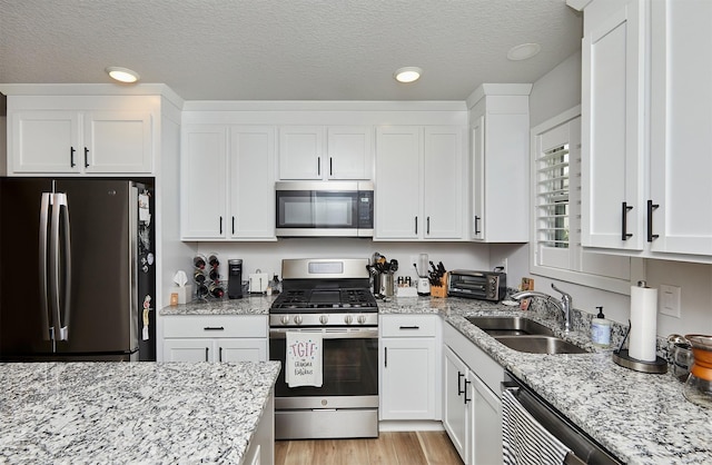 134 Aspen Dr, Norwalk, IA 50211 - kitchen featuring appliances with stainless steel finishes, a sink, white cabinetry, a textured ceiling, and light stone counters