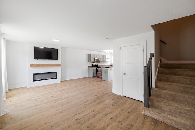 3605 Village Run Dr, Des Moines, IA 50317 - unfurnished living room with light wood-type flooring, stairs, a glass covered fireplace, and baseboards