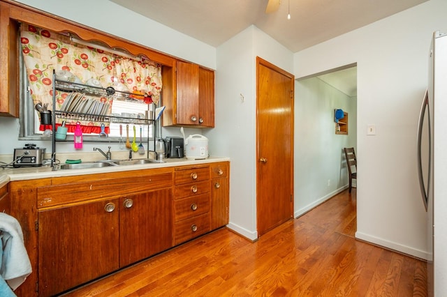 7409 Palm Dr, Urbandale, IA 50322 - kitchen with light wood-type flooring, light countertops, brown cabinetry, baseboards, and freestanding refrigerator