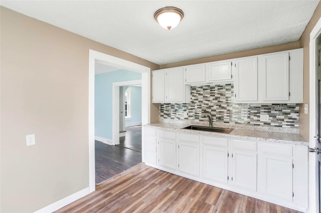 1127 10th St, Des Moines, IA 50314 - kitchen featuring a sink, tasteful backsplash, baseboards, white cabinets, and light wood-style flooring