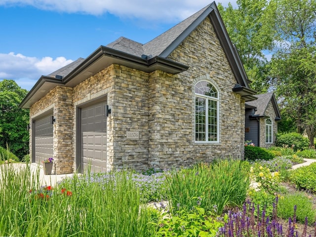 11576 NW Timberbrooke Ln, Grimes, IA 50111 - view of side of property featuring an attached garage, stone siding, and a shingled roof