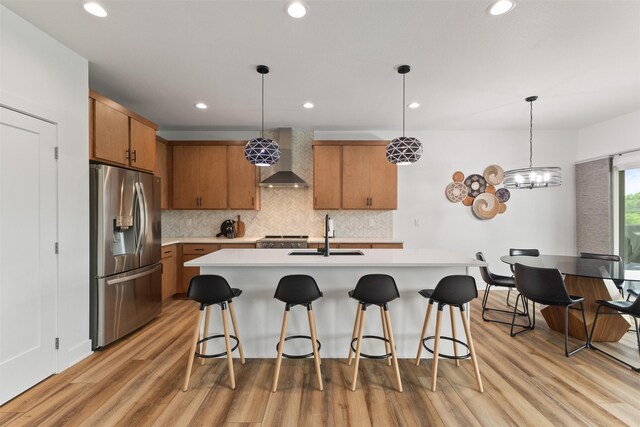 110 Bailey Cir, Waukee, IA 50263 - kitchen with stainless steel fridge, a sink, wall chimney range hood, light countertops, and brown cabinetry
