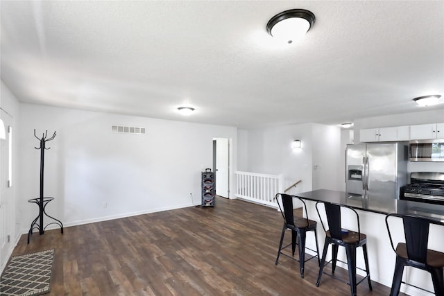 1908 E Walnut St, Des Moines, IA 50316 - kitchen with stainless steel appliances, a breakfast bar, dark countertops, dark wood-style flooring, and white cabinetry