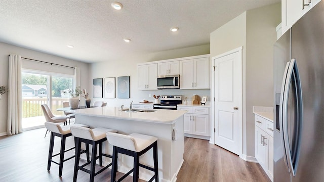 484 Kinley Dr, Waukee, IA 50263 - kitchen featuring stainless steel appliances, light wood-style flooring, a kitchen breakfast bar, a sink, and white cabinets