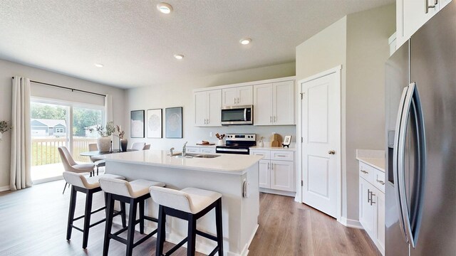 480 Kinley Dr, Waukee, IA 50263 - kitchen featuring stainless steel appliances, light wood-style flooring, a kitchen breakfast bar, a sink, and white cabinets