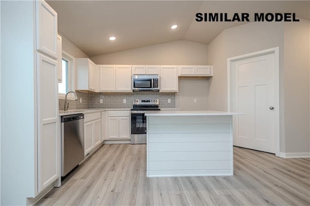 25088 Bluebird Cir, Adel, IA 50003 - kitchen with stainless steel appliances, decorative backsplash, light wood finished floors, white cabinetry, and vaulted ceiling