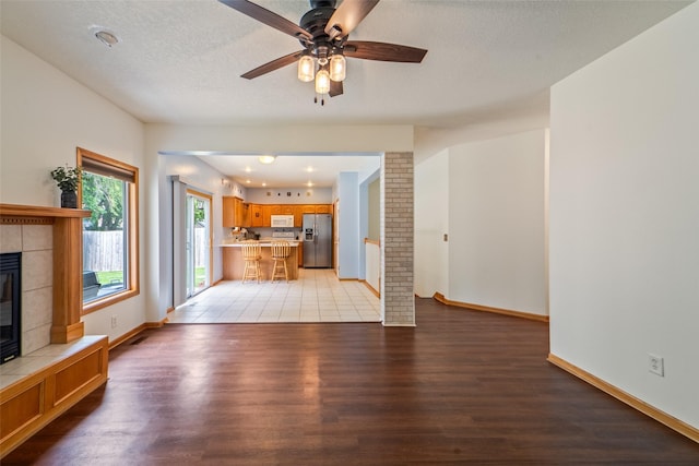 403 4th St NW, Altoona, IA 50009 - unfurnished living room with light wood finished floors, a fireplace, a ceiling fan, and a textured ceiling