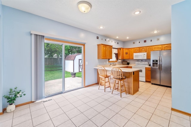403 4th St NW, Altoona, IA 50009 - kitchen featuring white appliances, a peninsula, light countertops, a kitchen bar, and brown cabinets