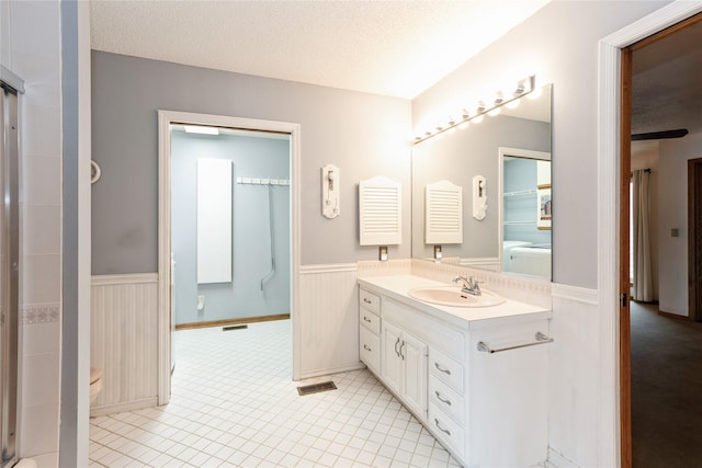 4922 Cedar Dr, West Des Moines, IA 50266 - bathroom featuring a wainscoted wall, vanity, a shower with shower door, tile patterned flooring, and a textured ceiling