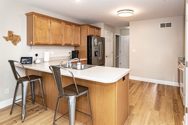 2732 Northridge Ln, Ames, IA 50010 - kitchen with stainless steel fridge, brown cabinetry, a peninsula, light wood-style flooring, and a breakfast bar area