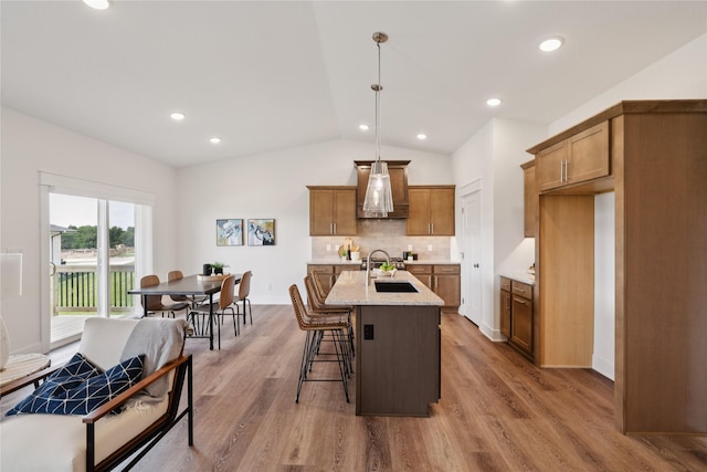 150 NW Hidden Knl, Waukee, IA 50263 - kitchen with brown cabinets, lofted ceiling, tasteful backsplash, wood finished floors, and pendant lighting