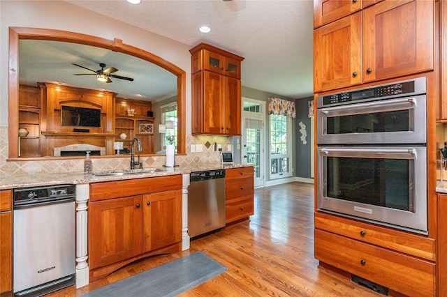 6725 NW 93rd St, Johnston, IA 50131 - kitchen featuring appliances with stainless steel finishes, ceiling fan, backsplash, light wood-style flooring, and brown cabinets