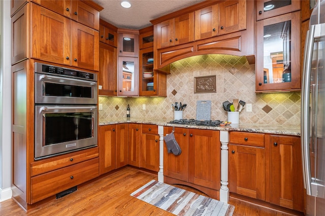 6725 NW 93rd St, Johnston, IA 50131 - kitchen with appliances with stainless steel finishes, brown cabinetry, light wood finished floors, backsplash, and a textured ceiling