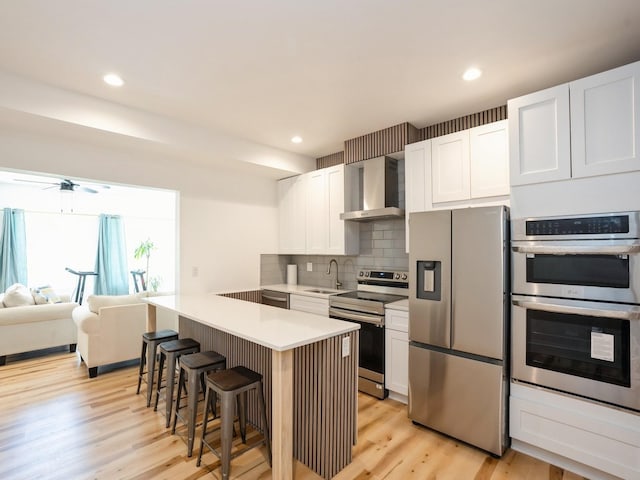 1010 Frederick Ave, Des Moines, IA 50315 - kitchen featuring stainless steel appliances, wall chimney range hood, a kitchen breakfast bar, tasteful backsplash, and light countertops