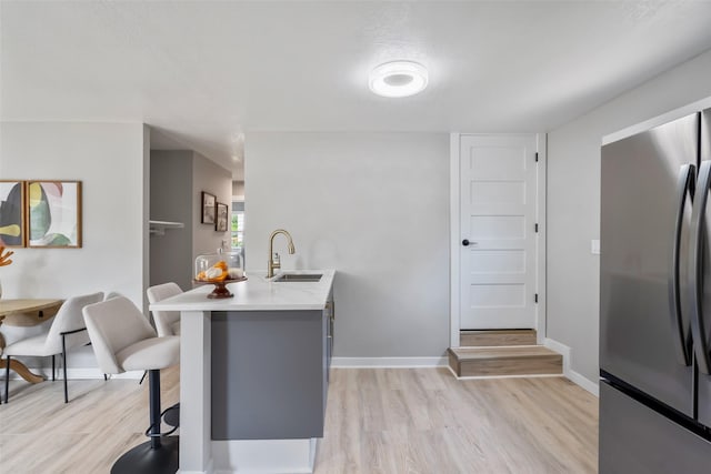 4127 E Seneca Ave, Des Moines, IA 50317 - kitchen with freestanding refrigerator, a kitchen bar, light wood finished floors, light countertops, and a peninsula