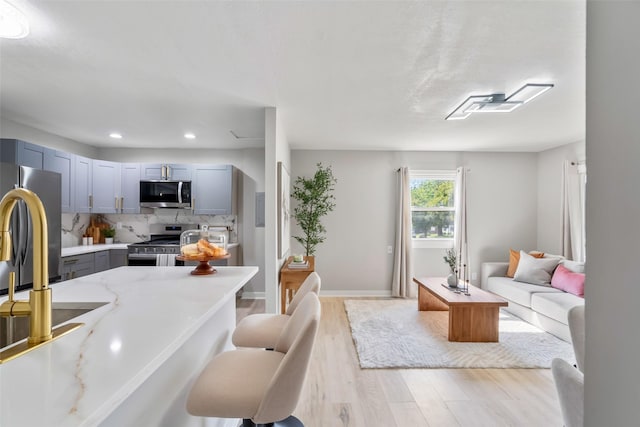 4127 E Seneca Ave, Des Moines, IA 50317 - kitchen with stainless steel appliances, gray cabinetry, light wood finished floors, tasteful backsplash, and a breakfast bar