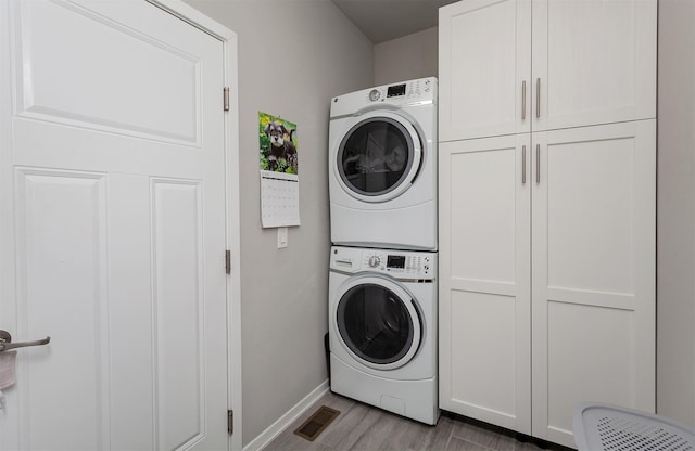 9180 Geanna Ct, West Des Moines, IA 50266 - laundry area featuring stacked washer and clothes dryer, cabinet space, and wood finished floors