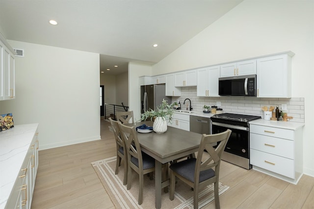 2004 Ammann Dr, Adel, IA 50003 - kitchen featuring stainless steel appliances, tasteful backsplash, light wood-type flooring, white cabinetry, and lofted ceiling
