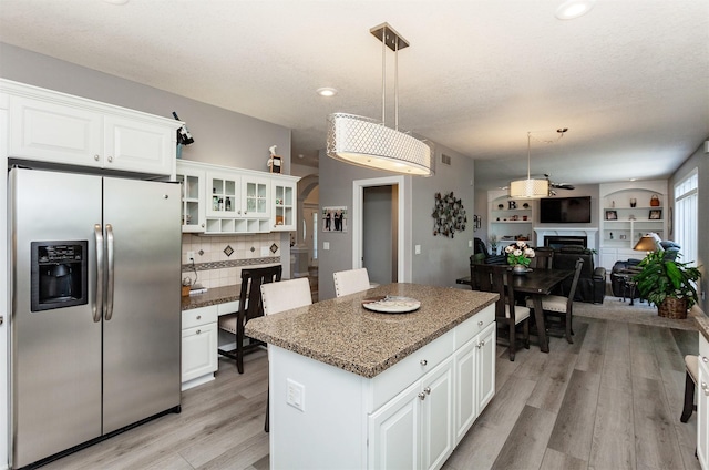 6511 NW 93rd St, Johnston, IA 50131 - kitchen featuring stainless steel refrigerator with ice dispenser, a fireplace, open floor plan, light wood finished floors, and a kitchen island