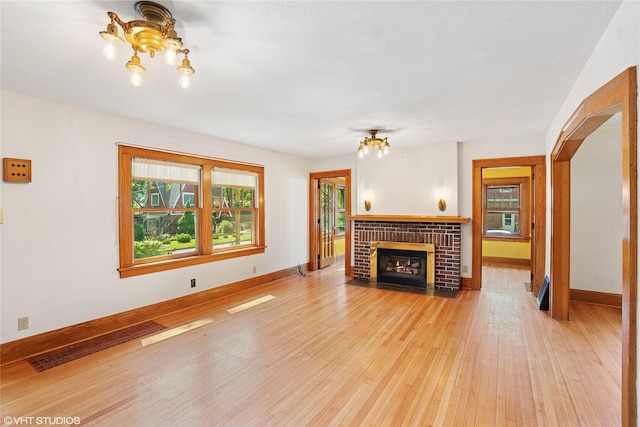 3320 SW 12th St, Des Moines, IA 50315 - unfurnished living room featuring a chandelier, light wood-type flooring, and a brick fireplace