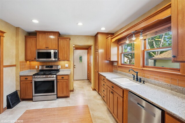 3320 SW 12th St, Des Moines, IA 50315 - kitchen featuring appliances with stainless steel finishes, backsplash, light stone counters, brown cabinetry, and recessed lighting