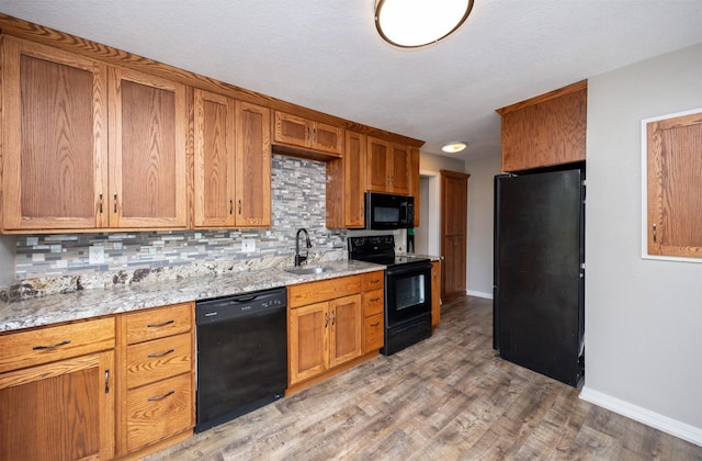 1012 28th St, Des Moines, IA 50311 - kitchen featuring black appliances, tasteful backsplash, brown cabinets, light wood-style floors, and light stone countertops